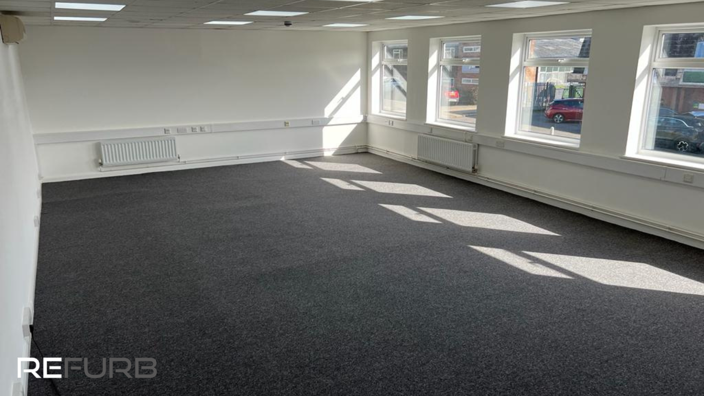 An empty, but freshly refurbished office with light coming through the windows onto the floor.