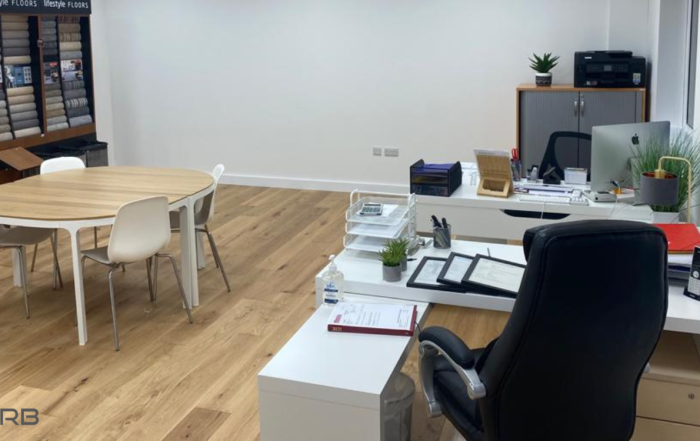An office after fit out. It shows a laminate floor a pair of desk, a central table with chairs around, and a display unit.